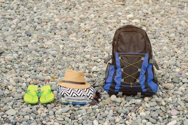 Chinelos, um chapéu, roupa e uma mochila em seixos. Conceito de viagem — Fotografia de Stock