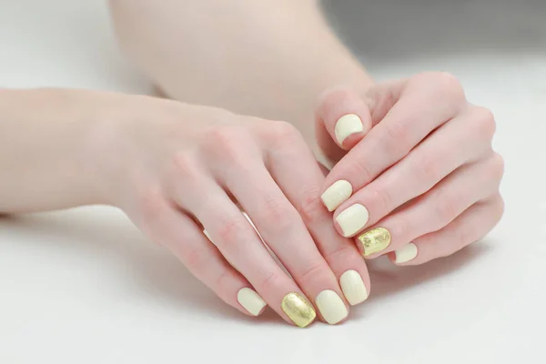 Schöne weibliche Hände mit einer Maniküre auf hellem Hintergrund. Gelb mit goldenen Nägeln — Stockfoto