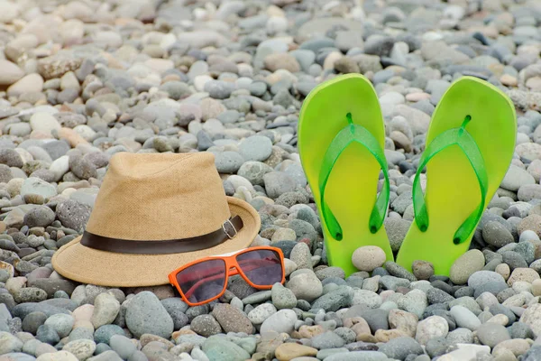 Hat, glasses and flip flops on a pebble beach, close-up. Recreation concept