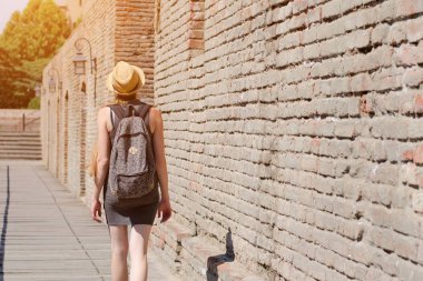 Kız şapka içinde ve şehir duvarı boyunca yürüyüş bir sırt çantası ile. güneşli gün