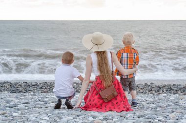 Anne ve sahilde oturan ve dalgaları seyretmekten iki oğlu. Arkadan görüntülemek