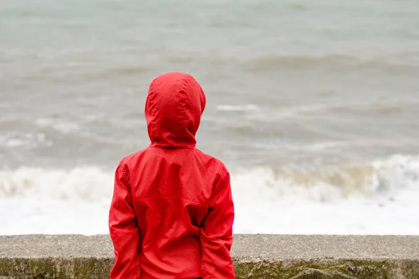 Hood duran dalgalar deniz arka plan üzerinde iskelede ile kırmızı ceketli çocuk — Stok fotoğraf