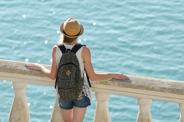 Balkonda duran ve denize bakarak şapkalı kız. Arkadan görüntülemek