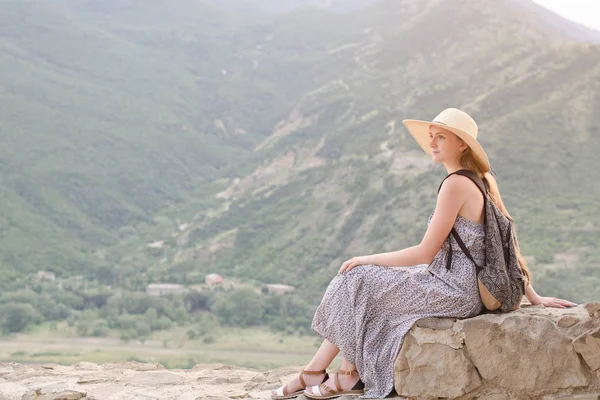 Geniş şapkalı Dağları nın arka plan üzerinde oturan bir sırt çantası ile güzel kız