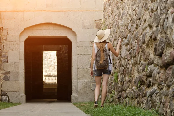 Kız şapka ve kalenin güneş ışığı yürüyüş bir sırt çantası ile. Arkadan Görünüm