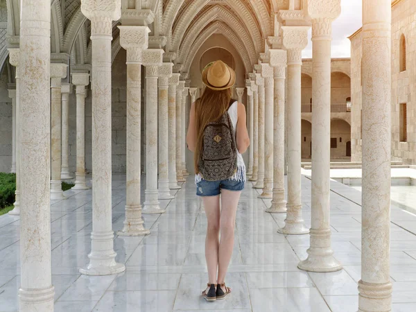 Sütunlar arasında bir sırt çantası konumu olan şapkalı kız. Arkadan Görünüm