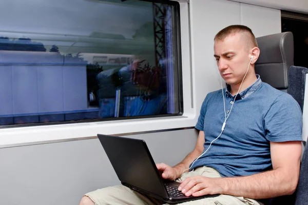 Young man working behind a laptop sitting in a train chair — Stock Photo, Image