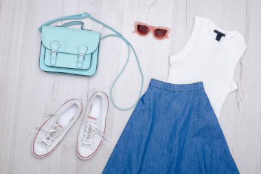 Kot etek, gözlük, beyaz spor ayakkabı, çanta ve üst. Moda kavramı. Ahşap arka plan.