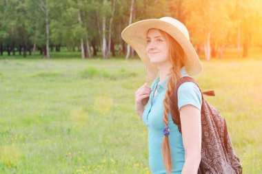 Sırt çantası ve şapka ile kız yaz orman karşı duruyor