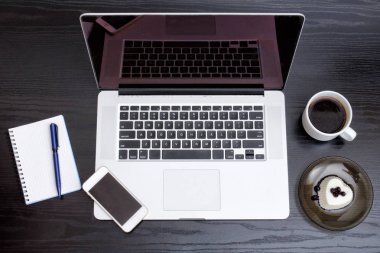 Açık dizüstü bilgisayar, akıllı telefon, kahve ve tatlı bir siyah arka plan üzerine bir fincan