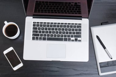 Açık dizüstü bilgisayar, grafik tablet, akıllı telefon ve kahve kupa siyah bir tabloda, üstten görünüm