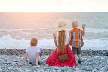 Anne ve sahilde oturan ve dalgaları seyretmekten iki oğlu. Arkadan görüntülemek