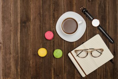 Kahve kupa, macarons, izle, defter ve ahşap bir masa üzerinde gözlük. Yan görünüm