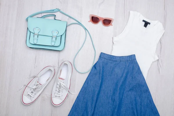 Kot etek, gözlük, beyaz spor ayakkabı, çanta ve üst. Moda kavramı. Ahşap arka plan.