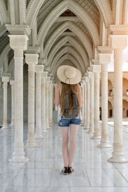 Sütunlar arasında bir sırt çantası konumu olan şapkalı kız. Arkadan Görünüm