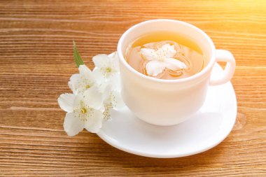 Beyaz bir fincan çay ile Yasemin ahşap bir masa üzerinde. Yakın, güneş ışığı