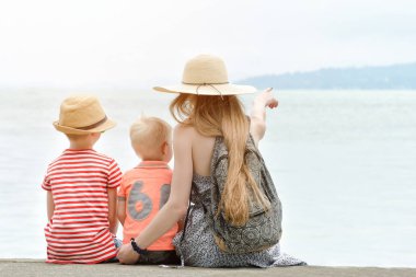 Anne ve iki oğlu iskelede oturup deniz ve dağlar mesafe hayranım. Arkadan Görünüm