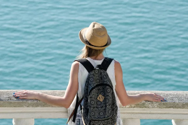 Kız şapka ve bir sırt çantası denizin üzerinde duruyor. Arkadan görüntülemek