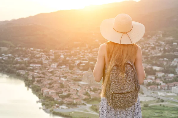 Güzel kız bir şapka ve bir sırt çantası ile şehir ve nehir aşağı bakar. Arkadan Görünüm