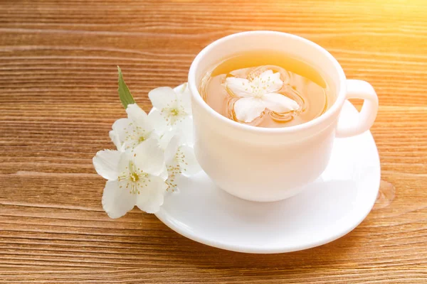 Beyaz bir fincan çay ile Yasemin ahşap bir masa üzerinde. Yakın, güneş ışığı