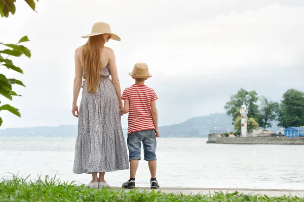 Anne ve oğlu deniz arka plan, deniz feneri ve dağlar uzakta iskelede tutuyoruz. Arkadan Görünüm