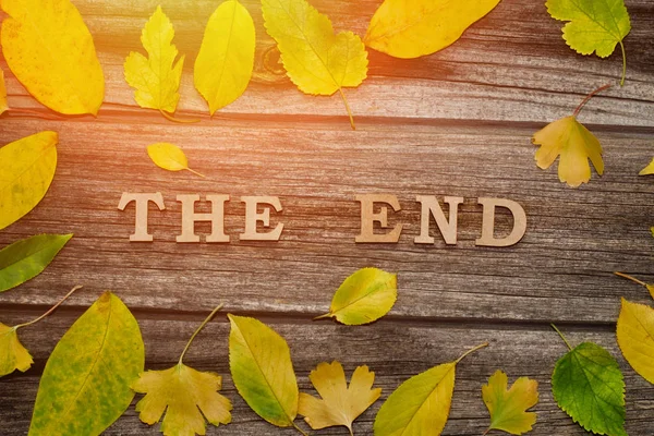 Inscription The end on a wooden background, frame of yellow leaves — Stock Photo, Image