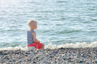 Boy Çizgili yelek içinde bir kaya denizin kenarında oturur. Arkadan Görünüm