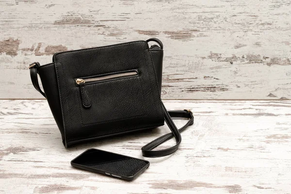 Маленькая черная женская сумка и телефон на деревянном фоне. Модная концепция — стоковое фото