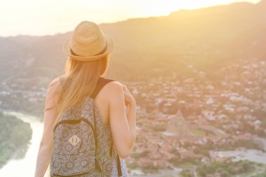 Güzel kız bir şapka ve bir sırt çantası ile şehir ve nehir aşağı bakar. Arkadan Görünüm