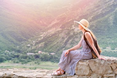 Geniş şapkalı Dağları nın arka plan üzerinde oturan bir sırt çantası ile güzel kız