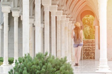 Sütunlar arasında yürüyen bir sırt çantası ile şapkalı kız. Arkadan Görünüm