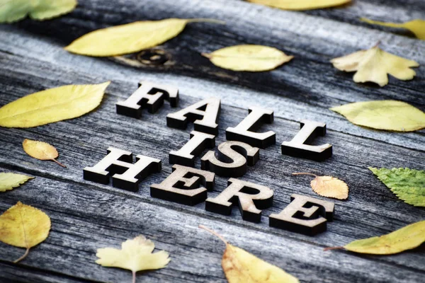 Inscriptie. Fall is hier, houten letters. Frame van gele bladeren, houten achtergrond — Stockfoto