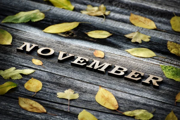 Mot de novembre, lettres en bois. Cadre de feuilles jaunes, fond en bois — Photo