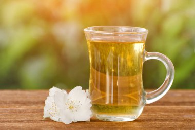 Şeffaf bir fincan çay ile Yasemin Yeşil, güneş ışığı bir arka plan üzerinde. Yakın çekim