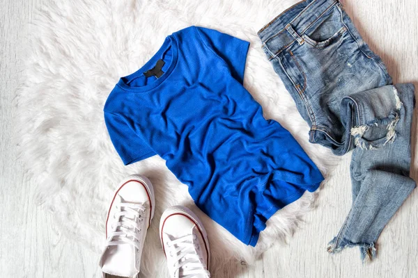 Blauw T-shirt, jeans en witte sneakers geript. Modieuze concept op wit bont — Stockfoto