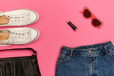 Kot şort, beyaz spor ayakkabı, siyah çanta, ruj ve gözlük. Parlak pembe arka plan. Moda kavramı