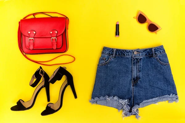 Short en denim, chaussures noires, sac à main rouge et lunettes. Fond jaune vif. Concept tendance — Photo