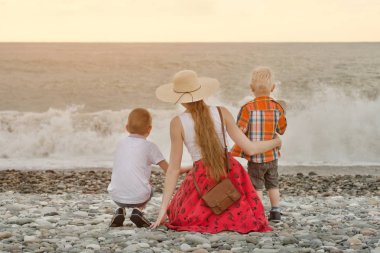 Anne ve sahilde oturan ve dalgaları seyretmekten iki oğlu. Arkadan görüntülemek
