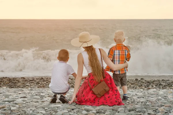 Anne ve sahilde oturan ve dalgaları seyretmekten iki oğlu. Arkadan görüntülemek