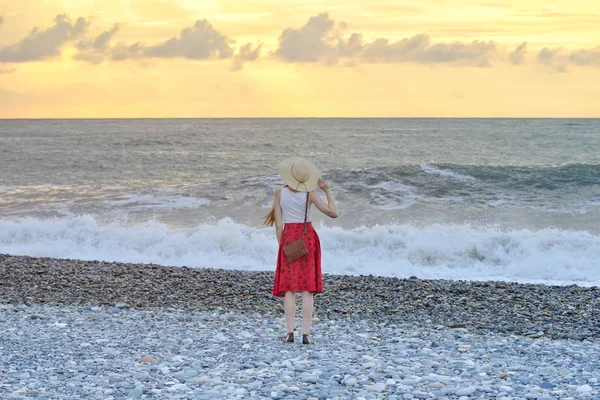 Kız şapka ve kırmızı etek ayakta sahilde günbatımı zamanı. Arkadan görüntülemek
