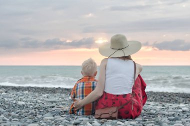 Anne ve oğlu okyanus kıyısında oturuyor. Arkadan görüntülemek