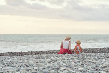 Anne ve oğlu sahilde oturuyor. Arkadan görüntülemek