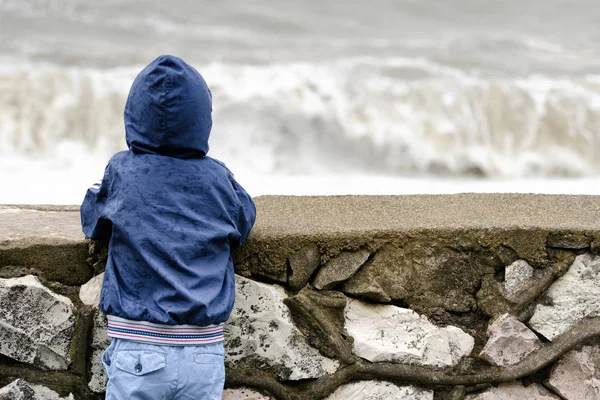 Pier deniz dalgaları arka planı sırtını ile hood ile mavi ceketli çocuk duruyor — Stok fotoğraf