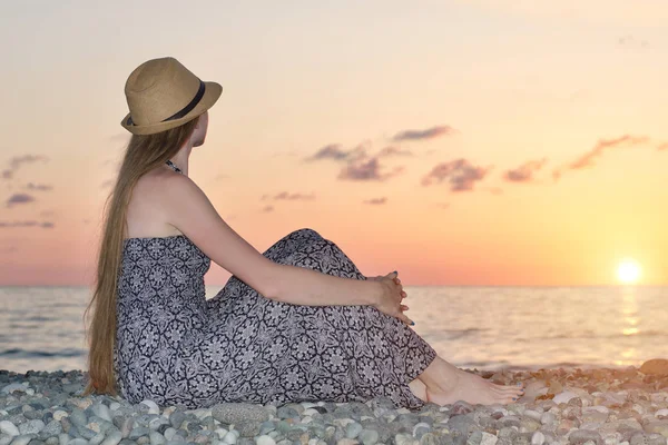 Gün batımında denize bir arka plan üzerinde oturan şapkalı kız