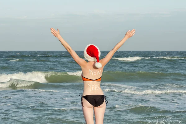 Mädchen in Weihnachtsmützen mit der Aufschrift Neujahr auf der Rückseite. Meeresküste. Hände hoch. zurück — Stockfoto