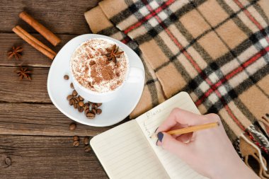 Bir kafede planlama. Kupa latte, içinde a defter bir kalem ile yazılı bir el. Üstten Görünüm