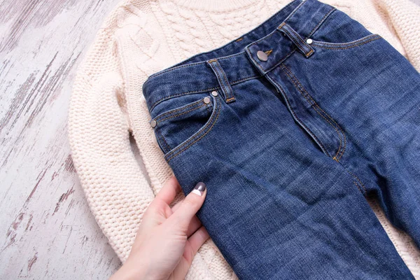 Mano femenina, suéter blanco y jeans sobre fondo de madera. Concepto de moda, vista superior — Foto de Stock