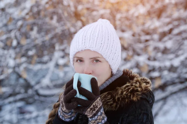 Chica con un sombrero blanco con una taza de té entre las ramas de los árboles cubiertos de nieve —  Fotos de Stock