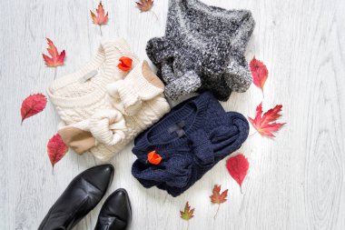 Üç kazak ve ahşap arka plan üzerinde siyah ayakkabılar. Kırmızı yaprakları. Moda kavramı.