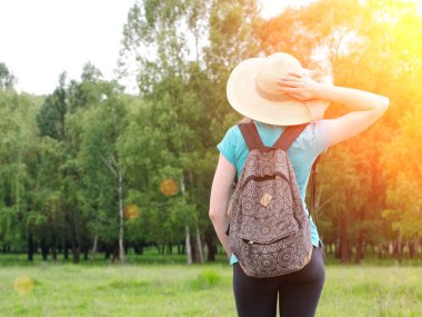 Kız şapka ve sırt çantası el ensenizdeki yeşil orman bir arka plan üzerinde tutar.